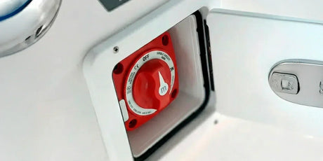 red marine battery selector switch with a white knob, mounted inside a white recessed box on a boat's hull